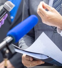 Reporter wearing protective gloves and face mask against coronavirus COVID-19 disease holding microphone at news conference during virus pandemic